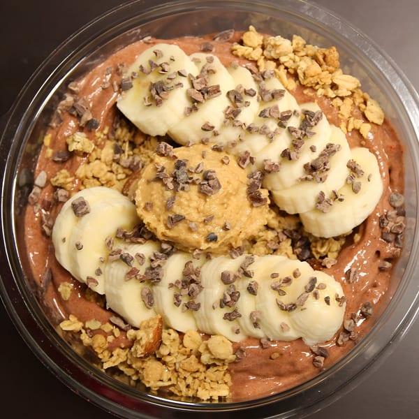A Jungle Bowl with chocolate smoothie base, banana slices, peanut butter, granola, and cacao nibs.
