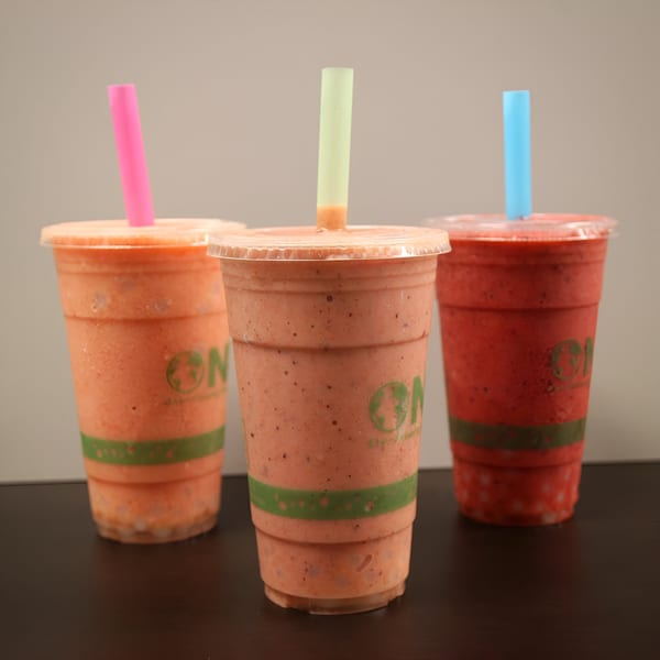 Three Jungle Bowl smoothies in clear cups with colorful straws, two orange and one red.