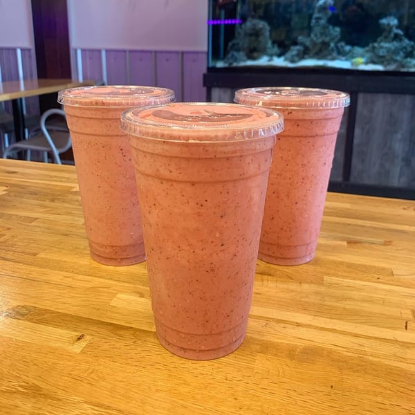 Three pink smoothies in clear plastic cups with lids on a wooden counter at The Jungle Bowl.