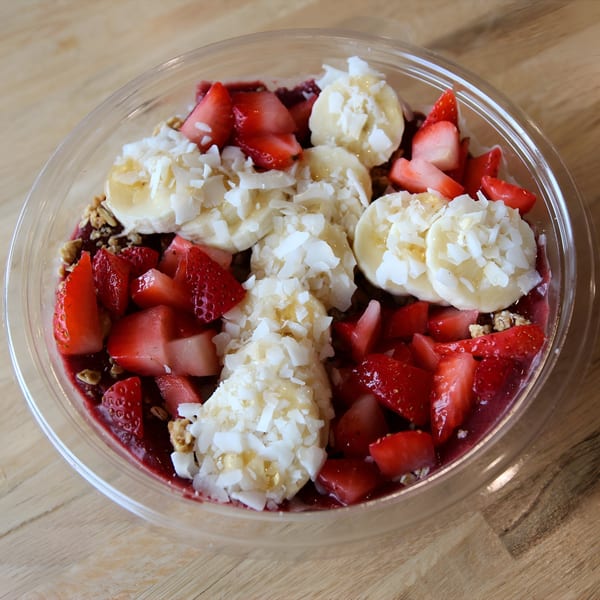 A Jungle Bowl acai bowl with strawberries, bananas, coconut flakes, and granola in a clear plastic container.