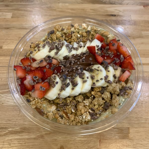A Jungle Bowl with granola, sliced bananas, strawberries, chocolate drizzle, and cacao nibs.