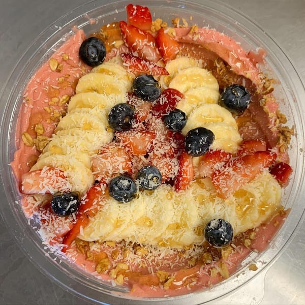 A vibrant Jungle Bowl with pink smoothie base, topped with bananas, blueberries, strawberries, coconut, and granola.