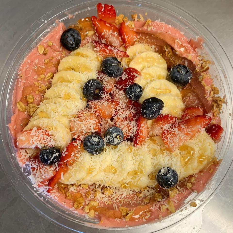 A vibrant Jungle Bowl with pink smoothie base, topped with bananas, blueberries, strawberries, coconut, and granola.