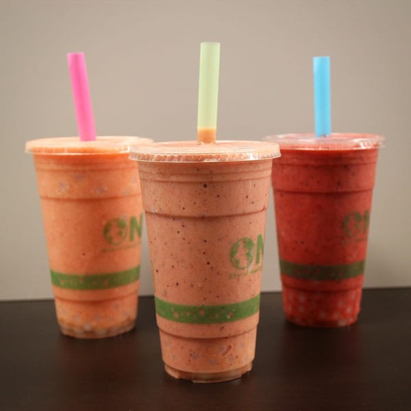 Three Jungle Bowl smoothies in clear cups with colorful straws on a dark surface.