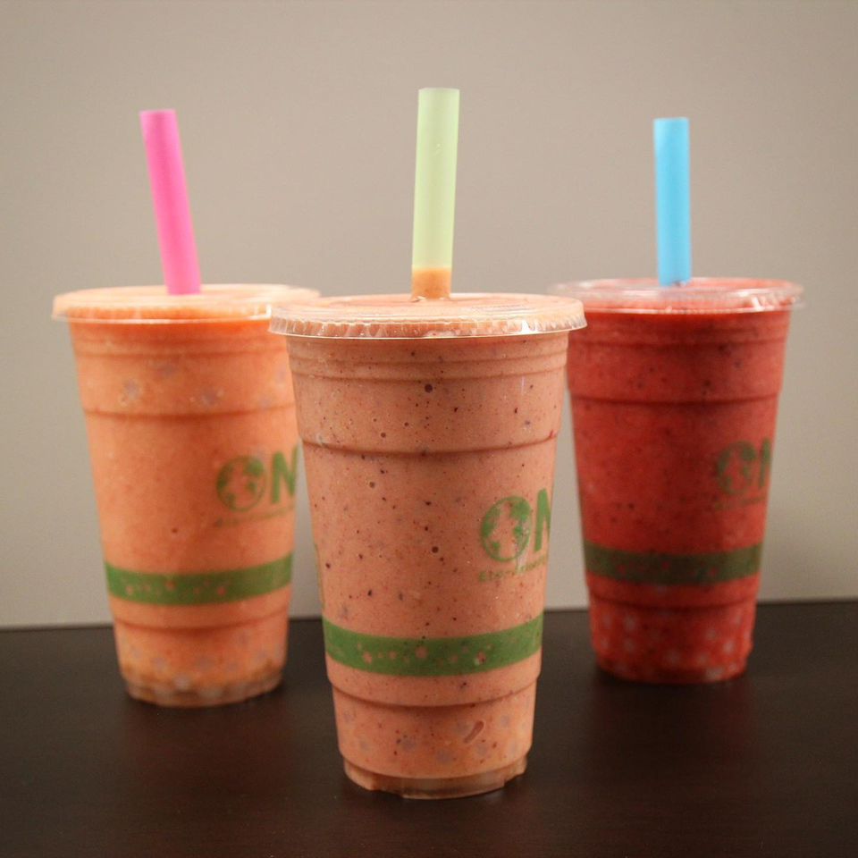 Three Jungle Bowl smoothies in clear cups with colorful straws on a dark surface.